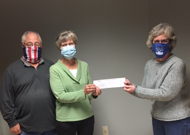 One man and Two women wear fabric face masks and hold between them a paper donation check.
