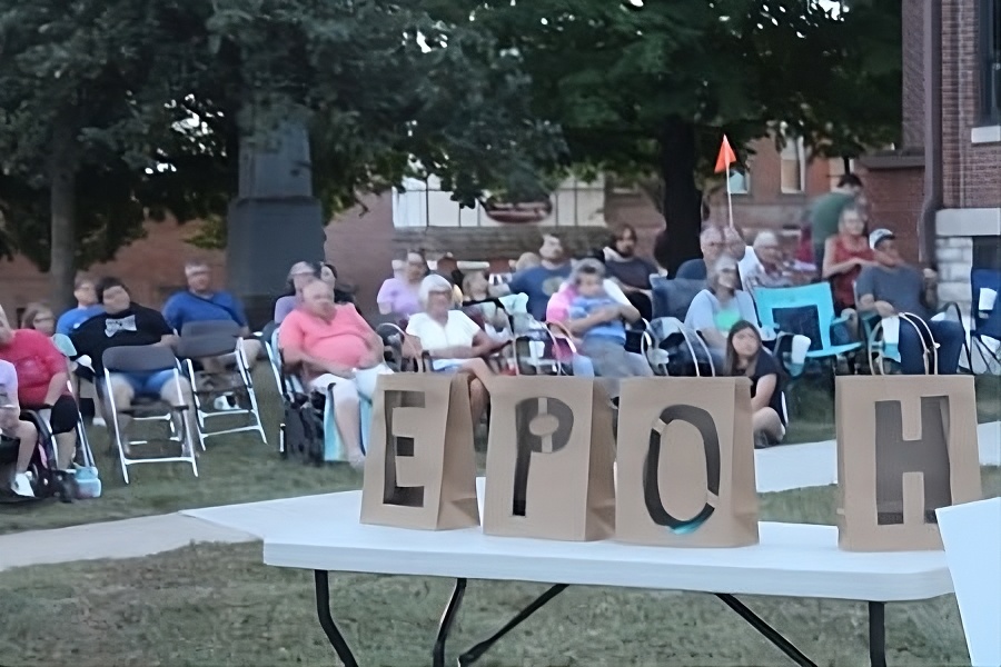 A diverse group of people on chairs, facing a sign that says HOPE, appearing friendly and engaged with each the outdoor program's speakers.