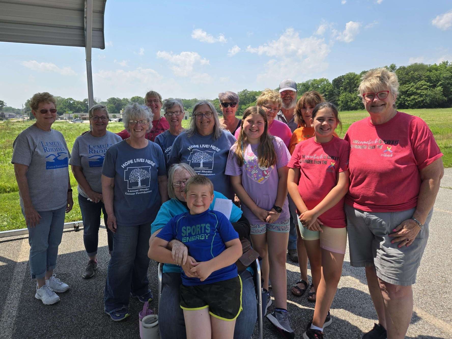 group of a dozen ladies and kids of all ages pose in a standing group outdoors all wearing colorful tee shirts branded with Lem Rhodes slogans
