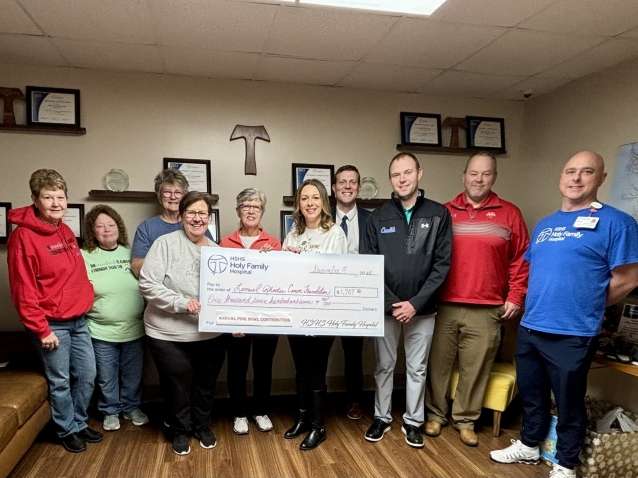 a group of ten men and women stand in a line in a hospital meeting room holding an oversized check made out to LRCF.