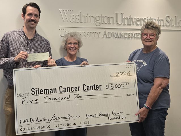 Three smiling adults hold an oversized check for Siteman Cancer Center sarcoma research, with Washington University signage behind them.