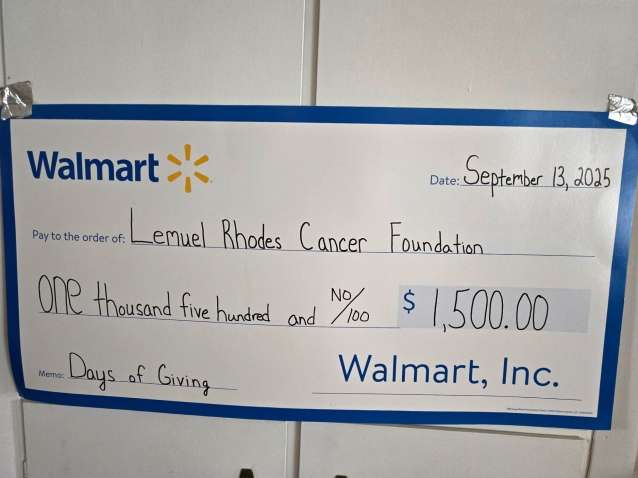 an oversized white rectangular check outlined in blue made out to Lemuel Rhodes Cancer Foundation from Walmart Incorporated