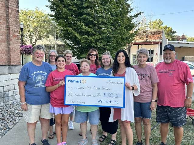 ten persons stand outdoors holding an oversized white rectangular check outlined in blue made out to Lemuel Rhodes Cancer Foundation from Walmart Incorporated