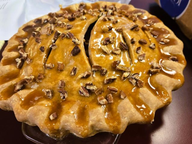 Golden, crimped pecan pastry covered in glossy caramel glaze and chopped nuts, creating a warm, indulgent snack for a great cause.